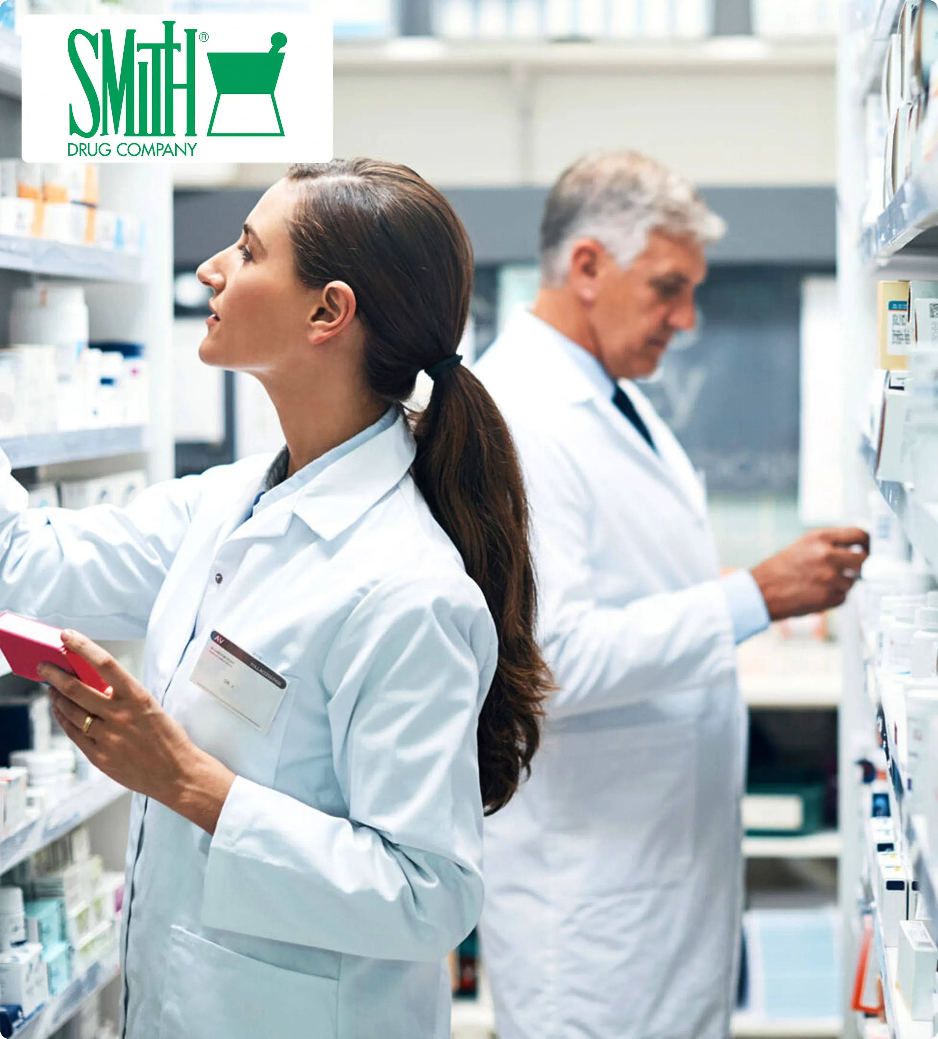 Two pharmacists in white lab coats stand beside shelves filled with medicine bottles. They are focused on inventory tasks, conveying professionalism.
