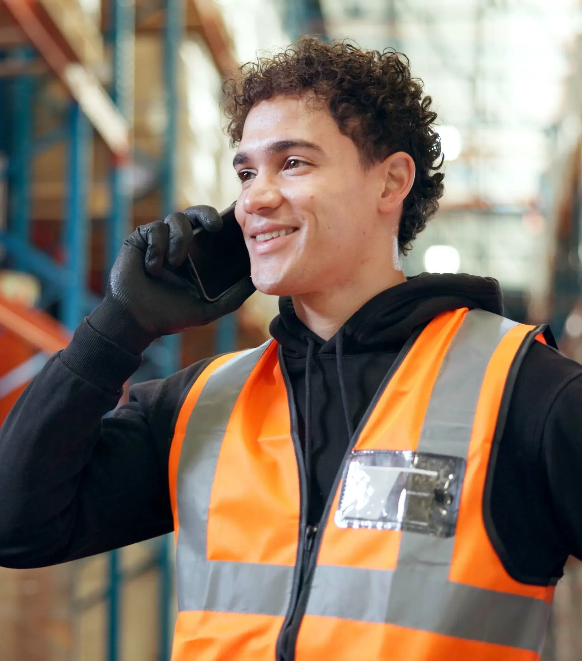 Person in a navy shirt wearing a headset carries a cardboard box in a warehouse, with shelves of boxes in the background suggesting busy activity.
